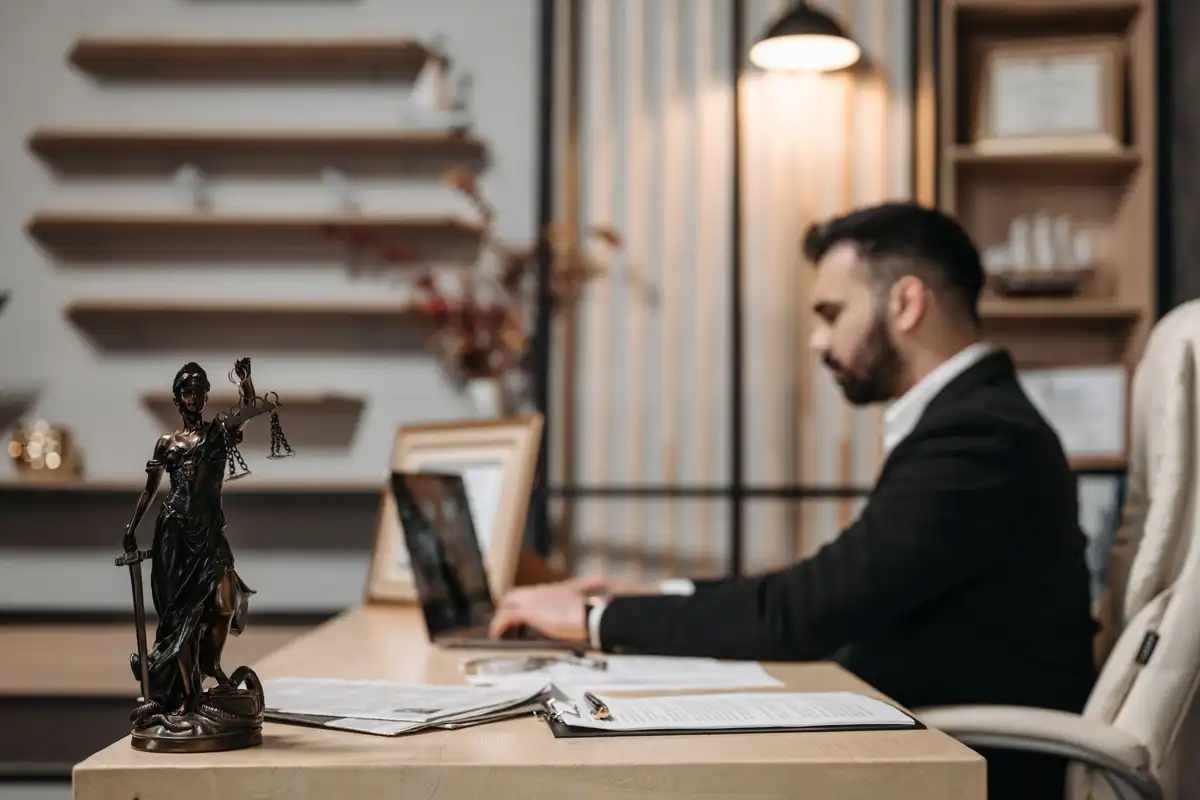 Avocat care lucrează la laptop într-un birou modern, cu statueta justiției alături