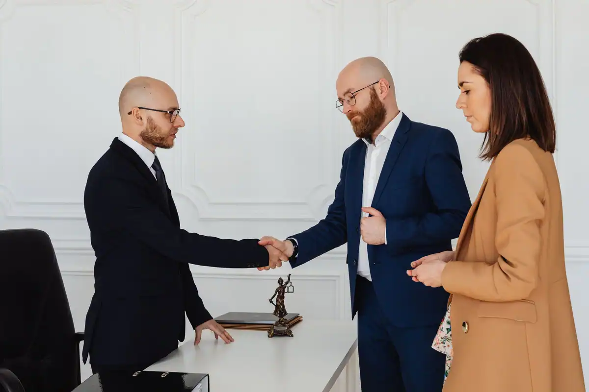 Trei profesioniști la costum își strâng mâna la începutul colaborării cu avocatul