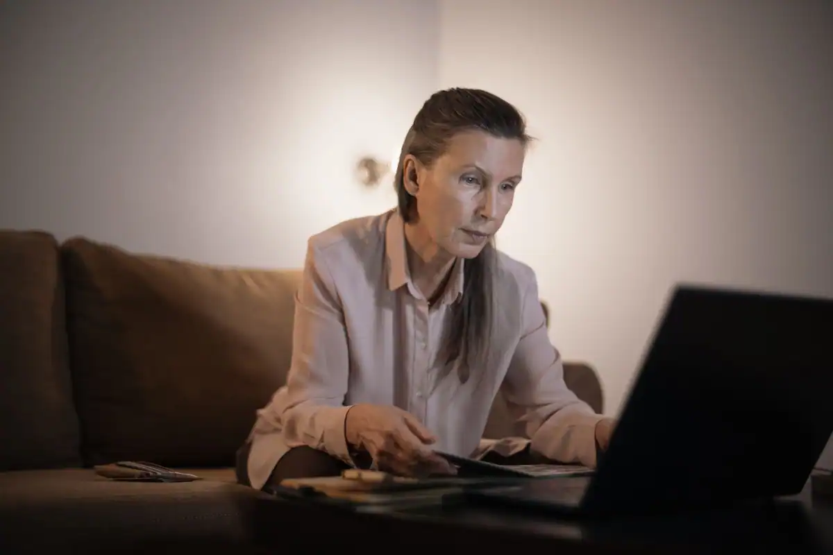 Femeie vârstnică ce lucrează la laptop în sufrageria ei, după pierderea soțului