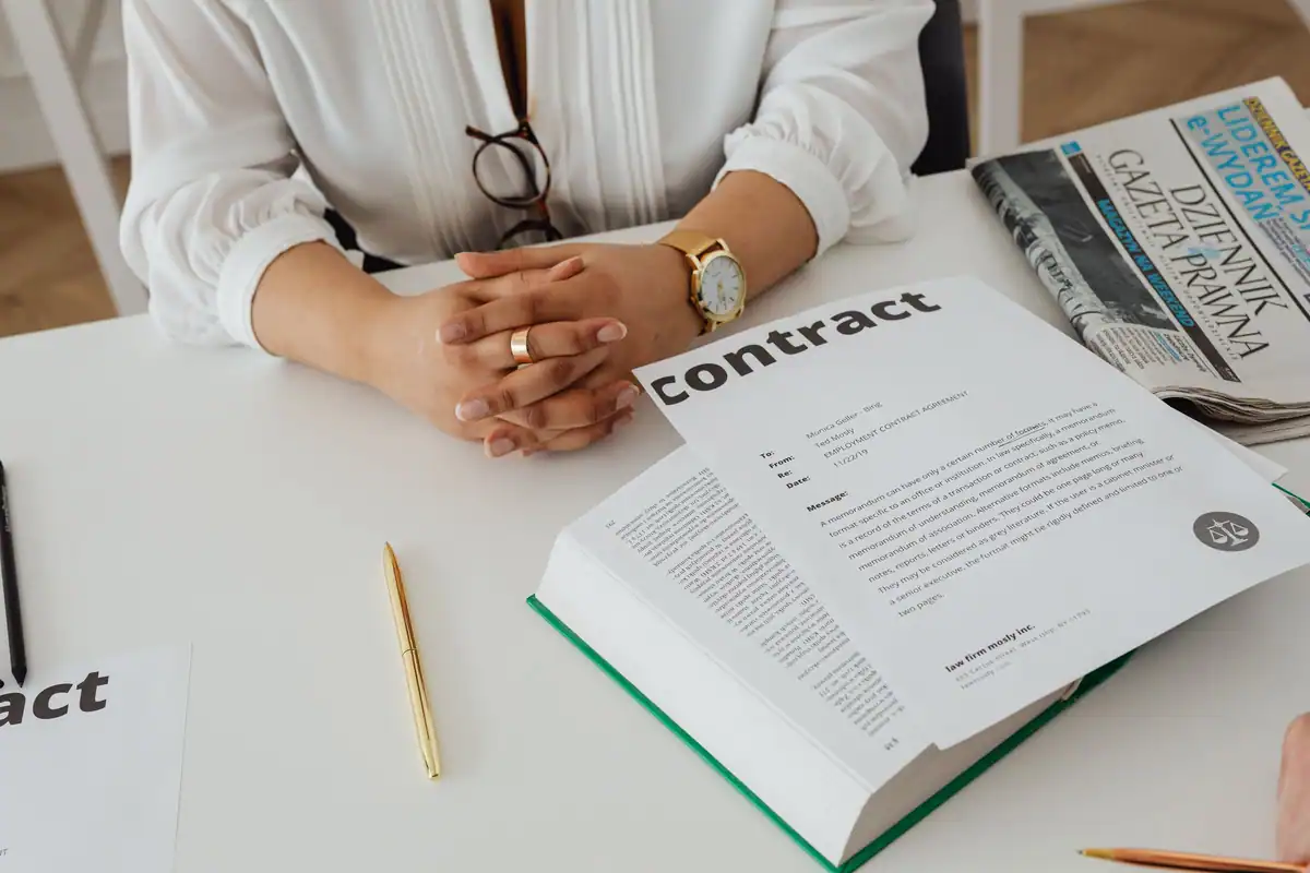 Femeie la birou care analizează un contract și actele juridice care îl însoțesc