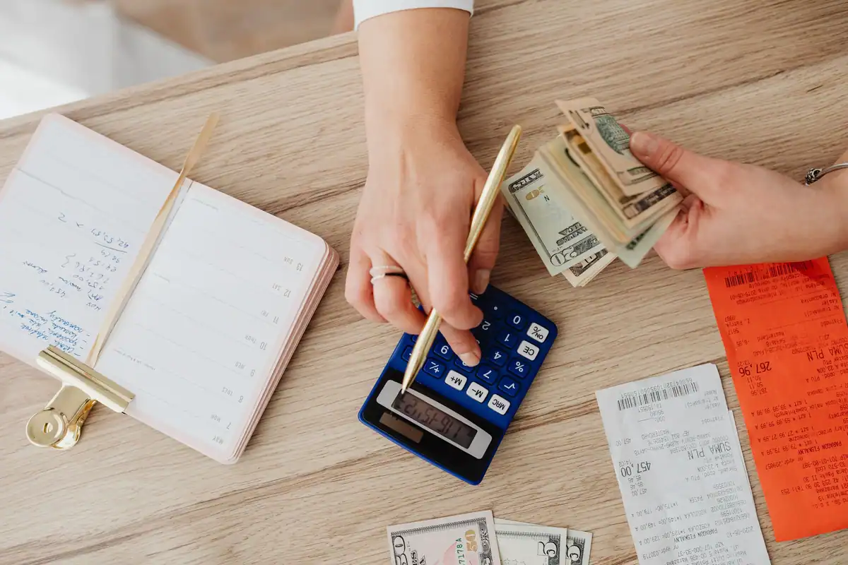 Mâini care socotesc bugetul cu calculator, bancnote și chitanțe pe o masă din lemn