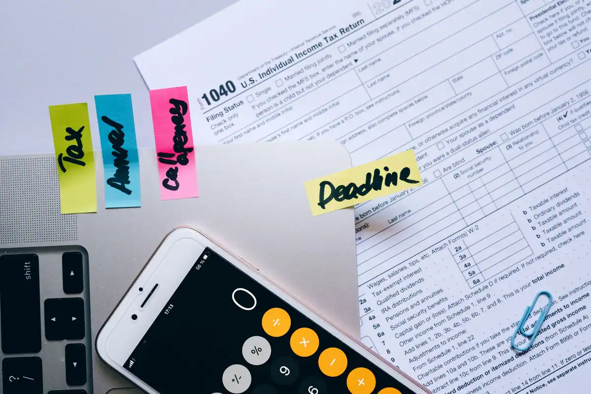 Birou cu documente fiscale, telefon cu calculator, notițe adezive și agrafe