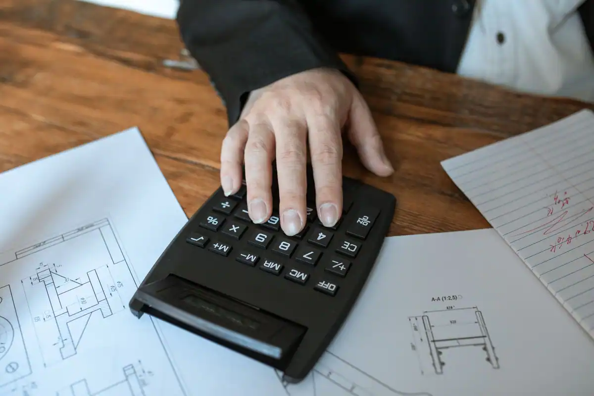 Mână care folosește calculatorul peste planurile unei case din masa succesorală