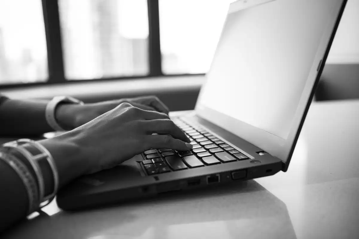 Mâini care tastează pe un laptop, fotografie alb-negru, căutare online în registre