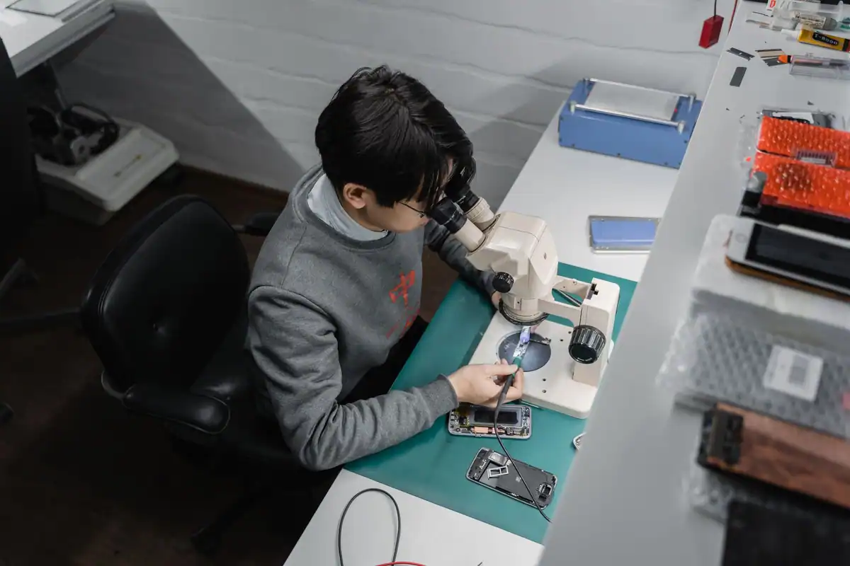 Tehnician care repară un telefon la microscop, descoperind un defect ascuns